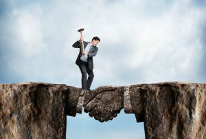 A businessman swings a sledgehammer at a land bridge connecting two cliffs as he tries to chip away at the metaphorical agreement represented by the bridge formed in the shape of a handshake.