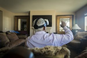 A senior black man using virtual reality headset technology in his living room, rear angle